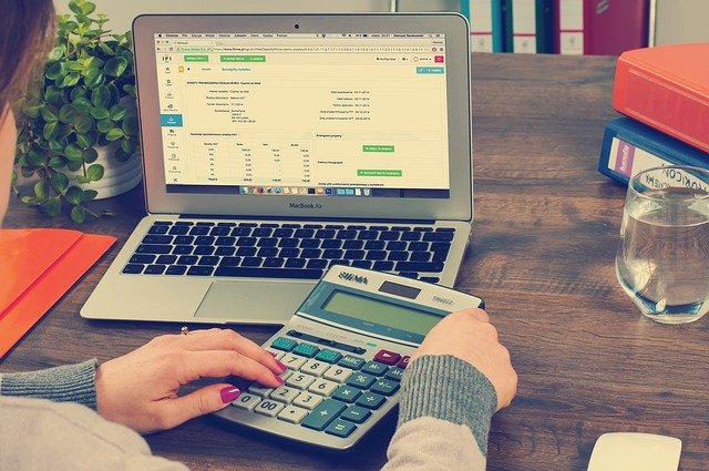  A person using a calculator and a laptop to check their annual financial reports in their online portal
