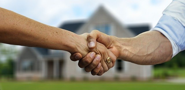 Two people shaking hands in the foreground with a blurred house in the background