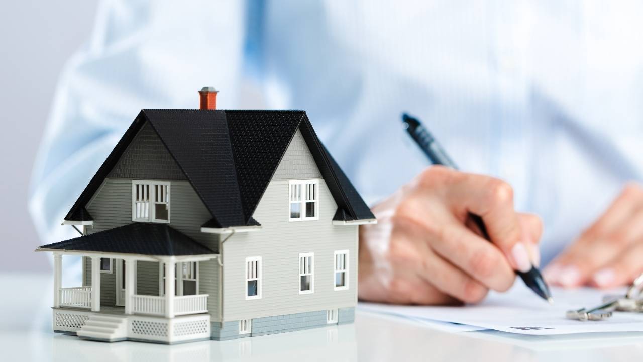 Cropped image of a person writing in a notebook behind a small model of a house