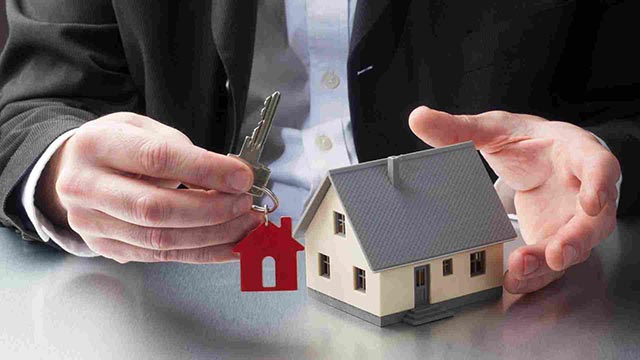 A person's hands holding a key and a small replica of a house